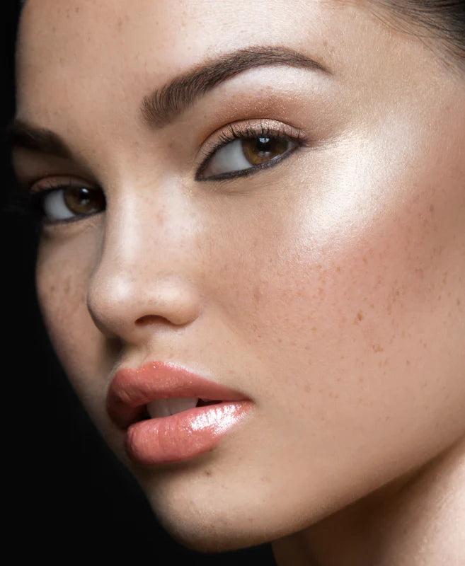 Close-up of a freckled woman with luminous skin and glossy lips.