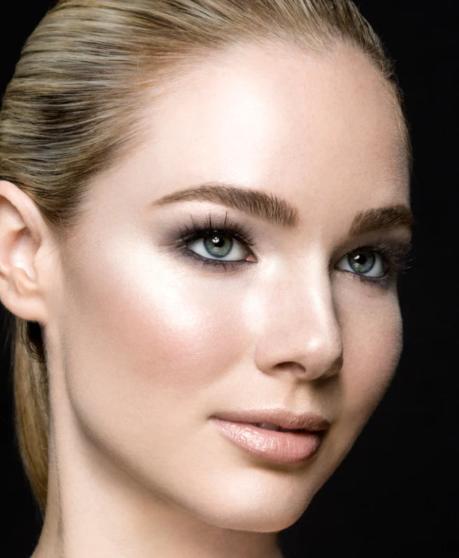 A blonde woman with a sleek ponytail, luminous complexion, and smoky eyes on a black background.