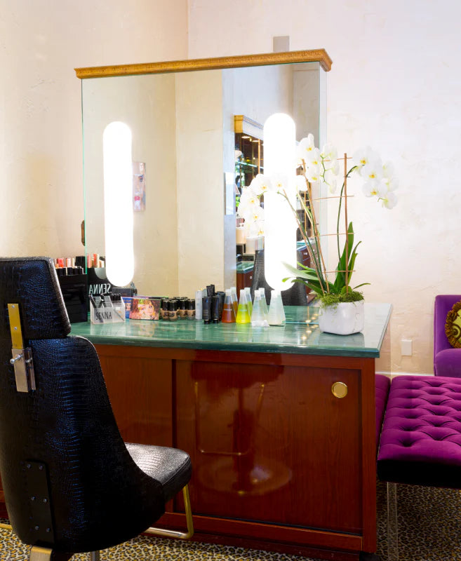 A makeup station with a lit vanity mirror, orchid arrangement, and seating in a salon setting.