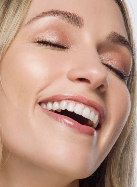 A smiling woman with shimmery eyeshadow and closed eyes, highlighting her radiant skin.